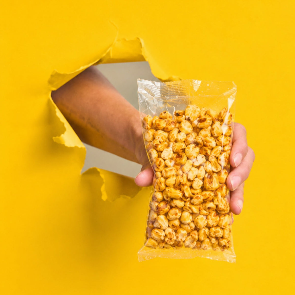 Mano sosteniendo una bolsa de maicitos de 50 g sin etiqueta sobre fondo amarillo