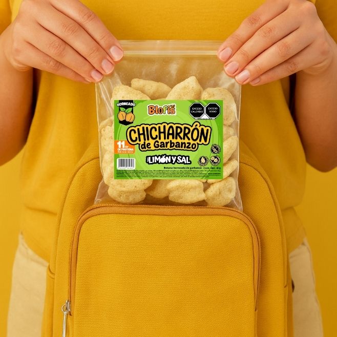 bolsita de chicharron de garbanzo horneado blofis sabor limon y sal saliendo de una mochila color amarillo con unas manos de mujer sosteniendo la bolsa