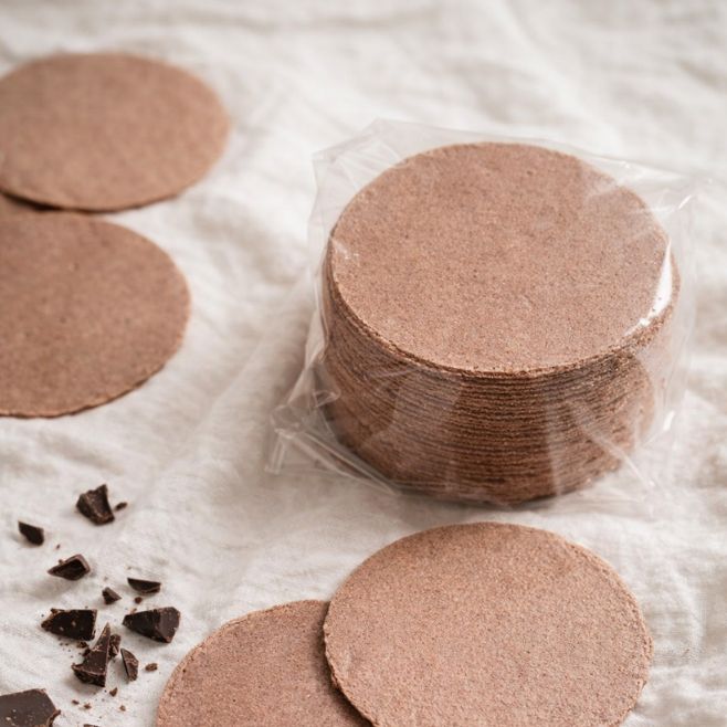 obleas de amaranto empaque de 60grs sobre mantel blanco junto a unos pedados de chocolates triturados