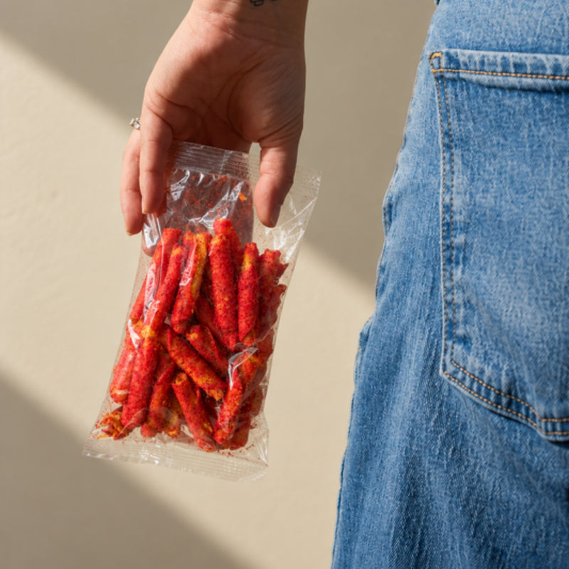 Bolsa transparente sin etiqueta con takitos de amaranto sabor Fuego, en la mano de una persona